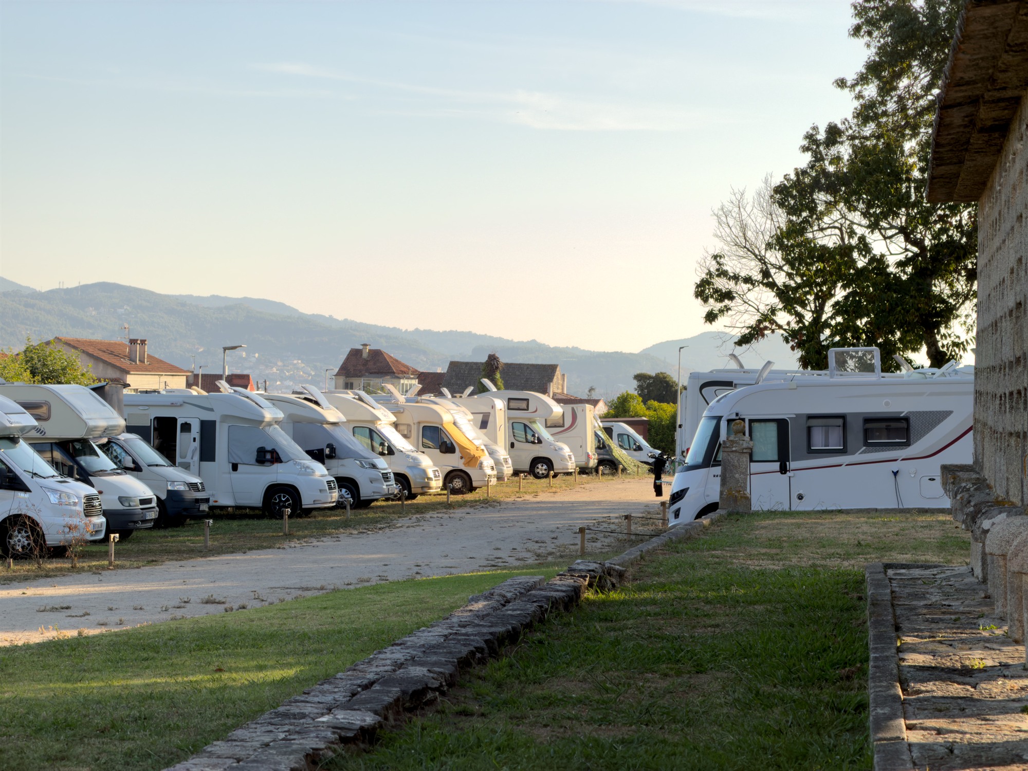 Fila de autocaravanas aparcadas en las plazas de Ledicia Camper Park con los montes del Val Miñor al fondo
